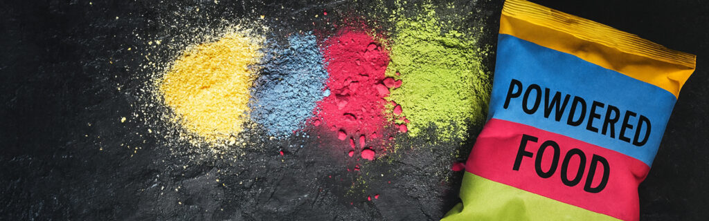 Colorful powdered food ingredients spilled on a dark surface next to a vibrant packaging pouch labeled “Powdered Food.”