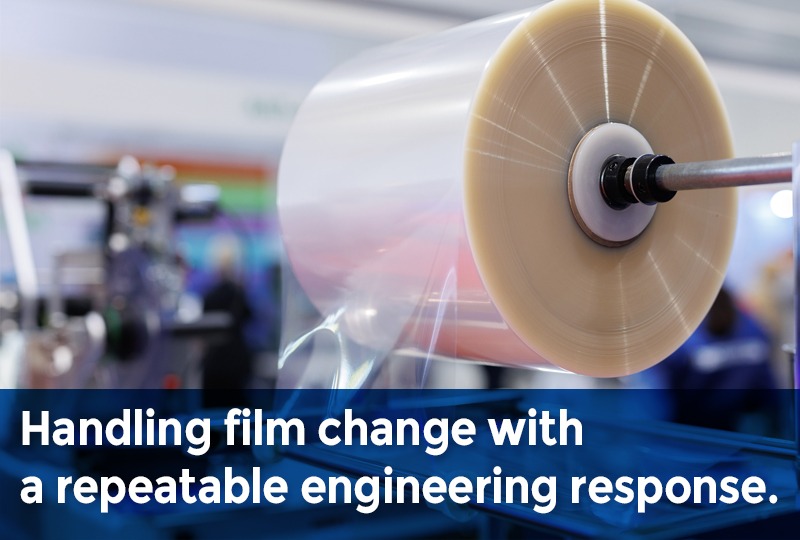 Large roll of flexible packaging film mounted on industrial equipment during a film change process.