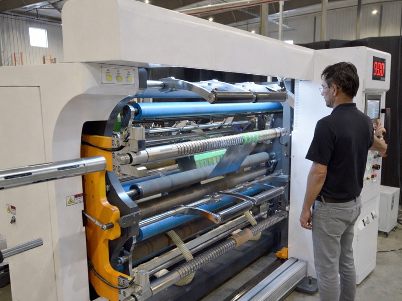 Industrial operator monitoring a high-precision film slitting machine processing plastic packaging film in a manufacturing facility.