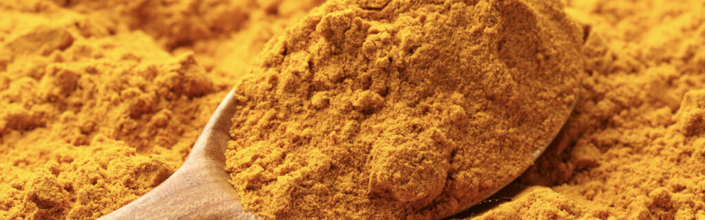 Close-up of bright turmeric powder in a wooden spoon, used in turmeric packaging applications