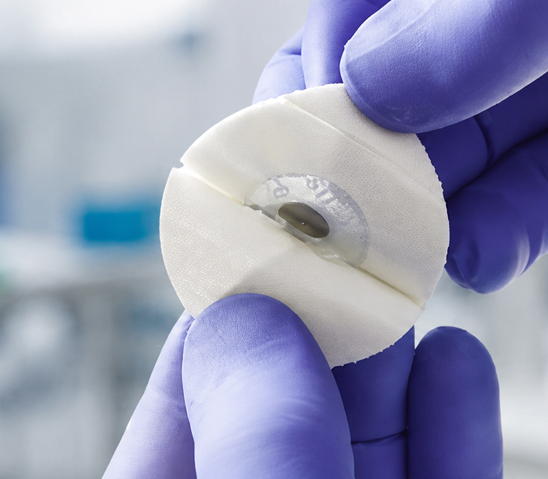Disposable EEG electrode held by a gloved hand alongside a sealed medical pouch for single-use EEG electrode packaging.